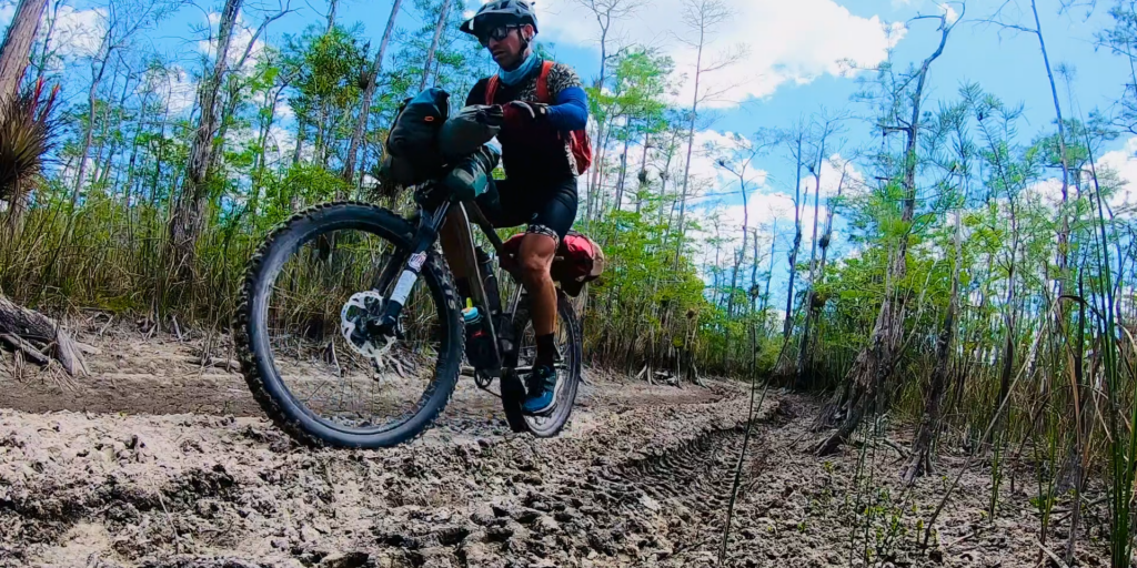 A man bikepacking down a dirt road in the Florida scrub.